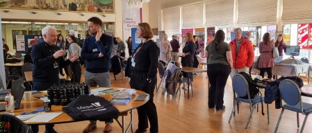 people at the Research marketplace event, having discussions around tables with promotional literature and banner stands